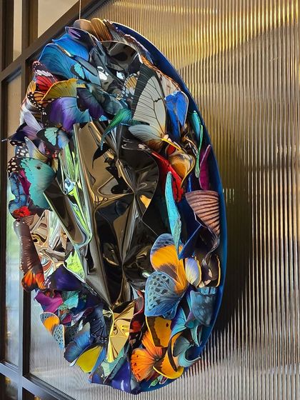 The "Metamorphosis in Metal" piece seen from the side, highlighting its texture and depth against a fluted glass wall.