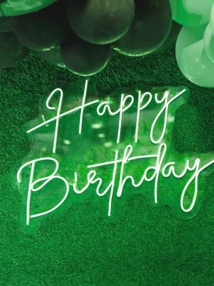 A neon "Happy Birthday" sign glowing against a green, turf-like backdrop, perfectly capturing the modern and exciting vibe of a football-themed party.