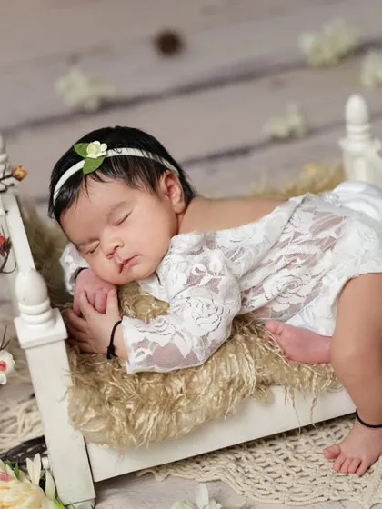 The classic 'tummy time' pose on a miniature bed, decorated with cherry blossoms. This pose beautifully shows the baby's delicate back and profile.