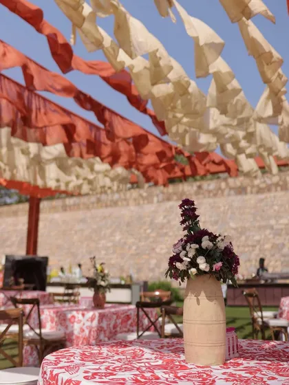 Guest seating with printed tablecloths under a ceiling of ruffled orange and cream drapes, set against the beautiful stone architecture of the venue.