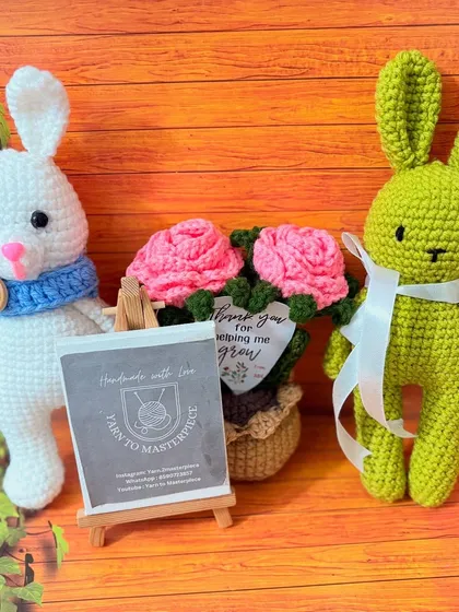 A pair of my handmade bunnies, one white and one green, posing with a pot of crochet roses. This shows how you can order them in different colors.