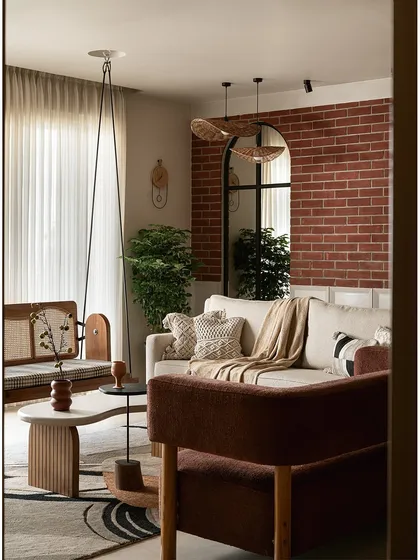 As you enter this living area, an exposed brick wall creates a warm, earthy backdrop. I placed a large arched mirror to reflect natural light, making the space feel larger and connected to the outdoors. The custom reversible cane swing, organic-shaped tables, and rich textures come together to create a grounded yet elegant feel.