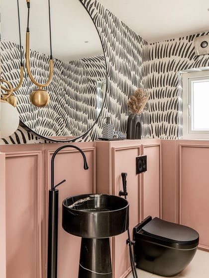 The powder room is a study in contrasts, with bold black-and-white wallpaper, pink paneling, and a striking black marble pedestal sink.