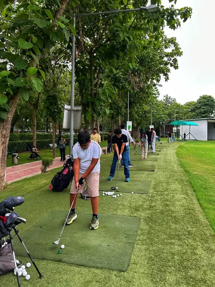 A young golfer in the foreground gets ready to swing, with the rest of the range busy behind him.
