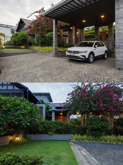 The entrance to the residence is lush and green, with a stone-paved driveway leading to a modern carport framed by bougainvillea.