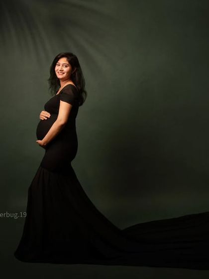 A simple yet stunning portrait of an expecting mother in a classic black mermaid gown. The dark green backdrop and subtle leaf shadow add a touch of natural elegance.