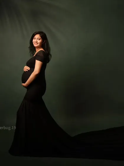 A simple yet stunning portrait of an expecting mother in a classic black mermaid gown. The dark green backdrop and subtle leaf shadow add a touch of natural elegance.