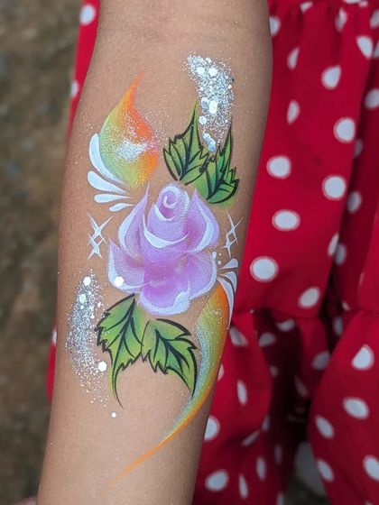 A stunning purple rose arm tattoo with a rainbow background and silver glitter.