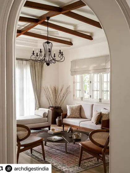 This view into the living room, captured by Architectural Digest, showcases the home's character. The design features exposed wooden ceiling beams, a classic chandelier, and a mix of modern and cane furniture, reflecting my philosophy of layering textures and eras.
