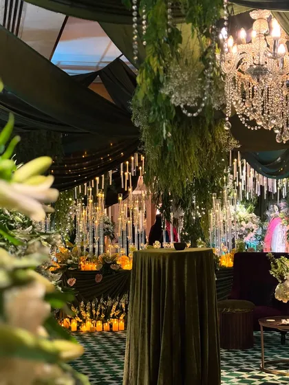 A view into the 'Enchanted Woods' theme, with a focus on the thousands of hanging and standing candles. The warm glow contrasts beautifully with the deep green drapery and lush foliage.