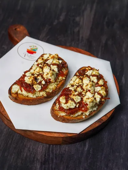 A moody shot of the feta and onion jam bruschetta, where the dark background enhances the rich colors of the toppings.