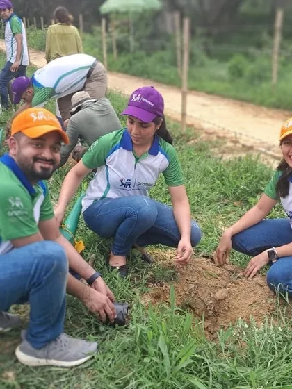 Three smiling volunteers from Aramco work together to plant a native sapling, showcasing the teamwork and positive energy of the day.