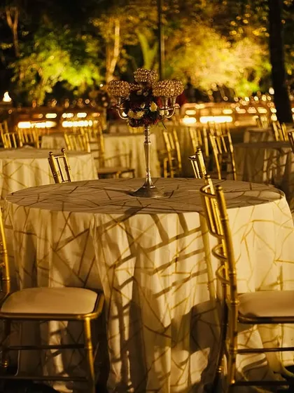 An elegant outdoor seating arrangement for a wedding reception. The golden chairs and classic table settings create a sophisticated ambiance for guests to enjoy their meal.