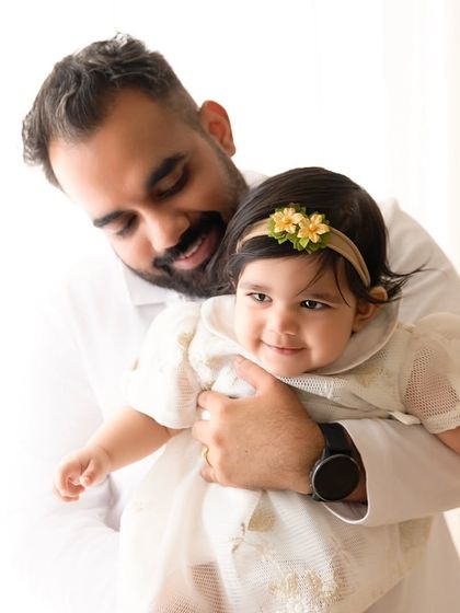 A father holds his smiling baby girl, looking down at her with affection.