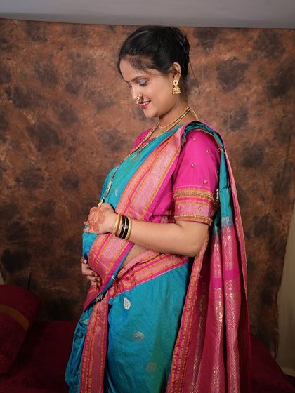 A side profile shot highlighting the baby bump, with the mom-to-be glowing in a traditional blue saree. The focus is on the beautiful details of the saree and her gentle expression.