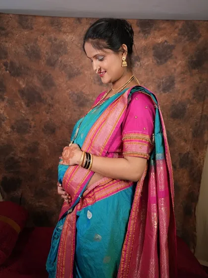 A side profile shot highlighting the baby bump, with the mom-to-be glowing in a traditional blue saree. The focus is on the beautiful details of the saree and her gentle expression.