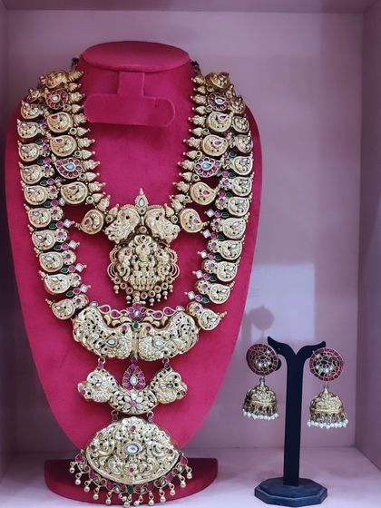 A heavy and ornate bridal set featuring multiple layers of temple jewellery and matching jhumkas.