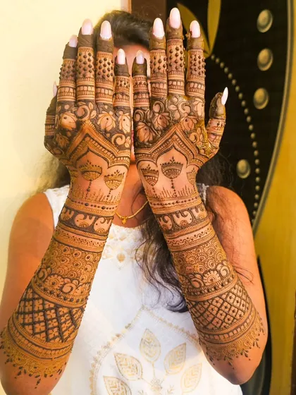 A bride playfully showing off her engagement henna, featuring hanging bells and other traditional motifs.