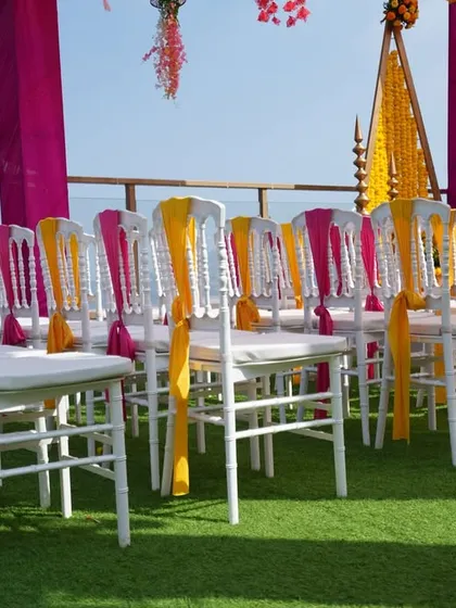 A closer look at the guest seating for the rooftop Haldi, with chairs elegantly decorated with pink and yellow sashes to match the overhead drapes.