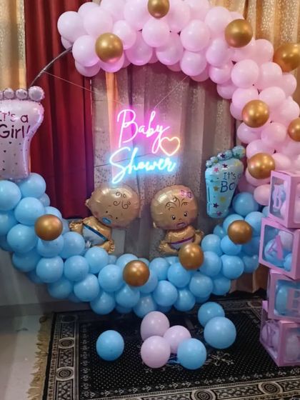 Another popular design for a baby shower or gender reveal. This setup features a circular balloon arch with blue on the bottom and pink on top, a neon sign, and "It's a Boy" and "It's a Girl" foot-shaped foil balloons.