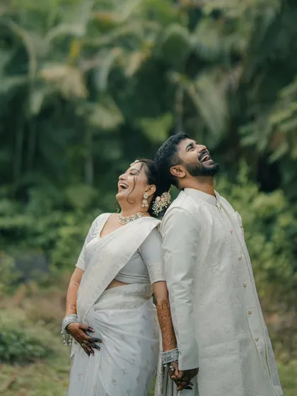 A moment of shared laughter between a couple in matching white outfits. The lush green background adds to the natural, joyful feel of this pre-wedding photo.