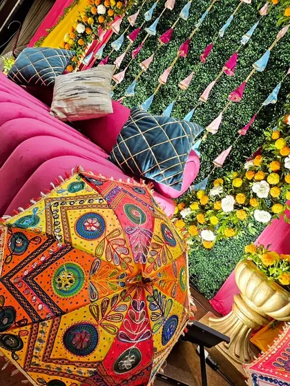 A detailed shot of our traditional Mehendi decor, showing the colorful Rajasthani umbrella and the plush pink seating against a backdrop of yellow and white flowers.