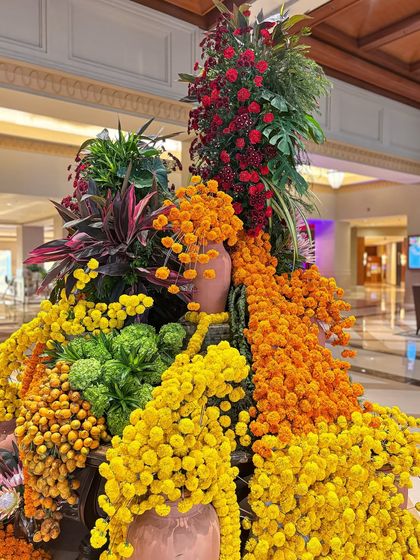 A stunning, large-scale floral arrangement designed to be a centerpiece in a grand lobby. It features a vibrant explosion of yellow and orange marigolds, accented with red blooms and lush greenery, capturing the essence of celebration.