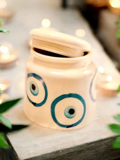This ceramic jar with a hand-painted evil eye design is both charming and useful. It can be used to store trinkets or as a decorative piece, bringing a touch of protection and artistry to any space.