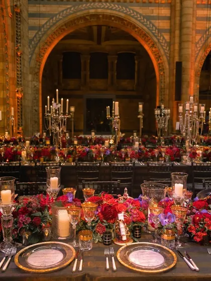 An opulent tablescape from the reception at the National History Museum, London. The rich red florals, gold-rimmed glassware, and candelabras create a look of pure luxury.