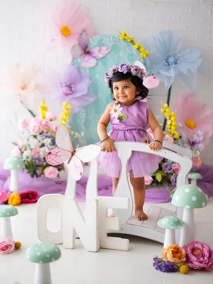 One year old and full of wonder! Standing on a bridge in a pastel fairy garden, this baby girl is celebrating her first birthday in the most enchanting way.