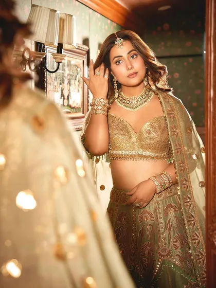 A moment of reflection. Hina Khan admires her complete look, featuring our handcrafted bridal jewelry, a perfect blend of tradition and modern luxury.