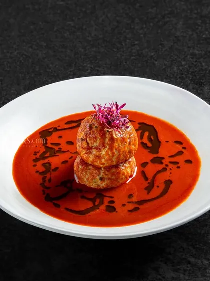 Koftas served in a rich, red gravy. The deep colors and minimalist plating give this dish a dramatic and appealing look.