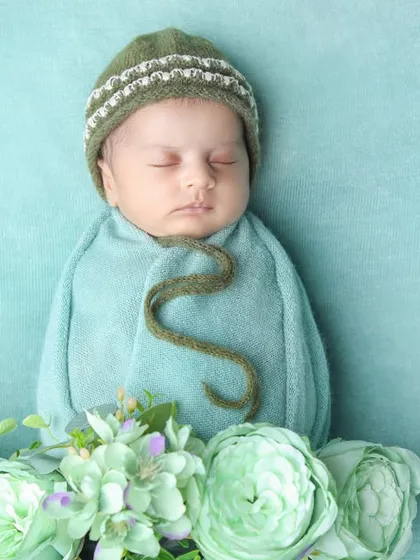 Fresh out of dreams and wrapped in cuteness, this newborn is surrounded by soft green flowers.