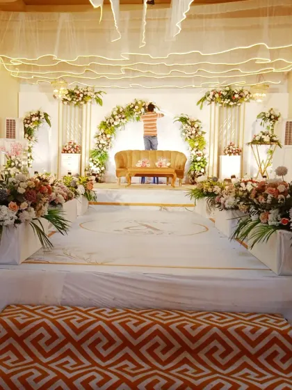 A behind-the-scenes look at my team setting up a white and gold themed stage in a hall, ensuring every floral detail is perfect.