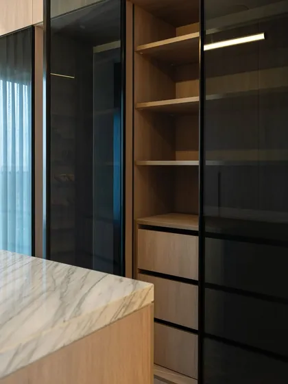 The combination of dark tinted glass doors and warm wood interiors creates a sophisticated and modern look for this wardrobe. The glass offers a subtle glimpse of the contents while maintaining a sleek, clean aesthetic.