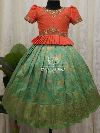 An elegant peplum-style Pattu Pavadai. The orange blouse with gold embroidery is beautifully contrasted with a sea-green Banarasi brocade skirt.
