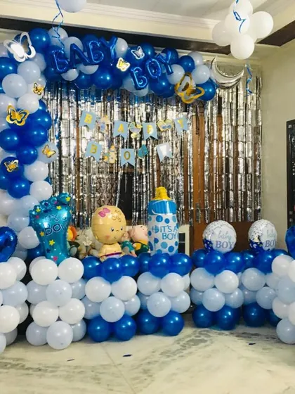 A full 'Welcome Baby Boy' decoration at home. The setup includes a balloon arch with a silver shimmer curtain and multiple balloon pillars with baby-themed foils.
