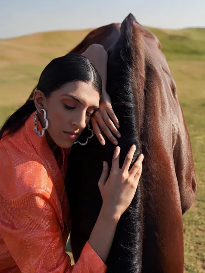 A model in a vibrant orange suit embraces a horse in a grassy field. This image shows the versatility of our landscape, suitable for creating bold and colorful fashion statements.