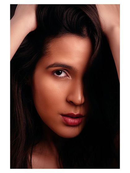 A close-up beauty portrait with a focus on the model's expressive eyes and soft features. The lighting is warm and intimate.