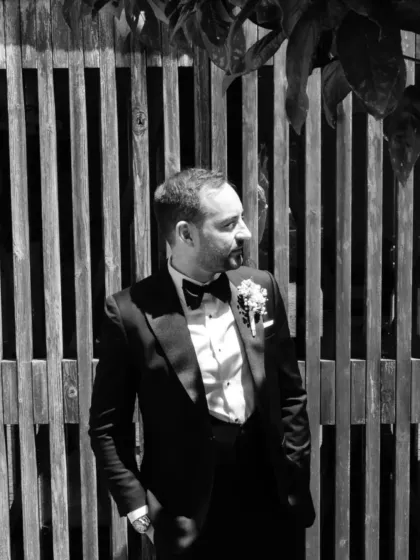 A timeless portrait of a groom in his bespoke black tuxedo. This black-and-white shot emphasizes the sharp silhouette and classic appeal of a perfectly tailored suit, crafted to make memories that last a lifetime.