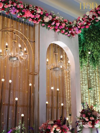 A beautiful detail of a floral and light installation, with chandeliers and light bulbs peeking through arches and greenery.
