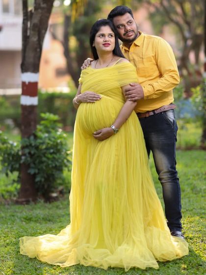 A lovely couple's portrait in a park. The yellow maternity gown brings a pop of color, and the partner's matching shirt makes for a well-coordinated and sweet photo.