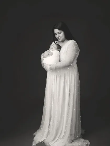 A stunning black and white portrait of a mother holding her newborn. Her elegant dress and the simple, dark background create a feeling of timeless grace.