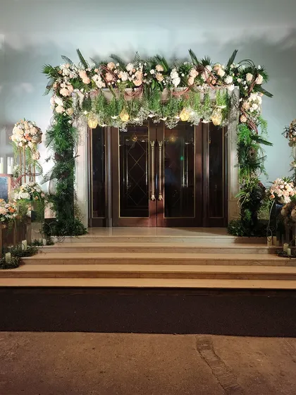 A beautiful floral archway at the top of a staircase, creating a picture-perfect entrance. The arrangement uses soft peach and white flowers with plenty of greenery for a romantic, garden-like feel.