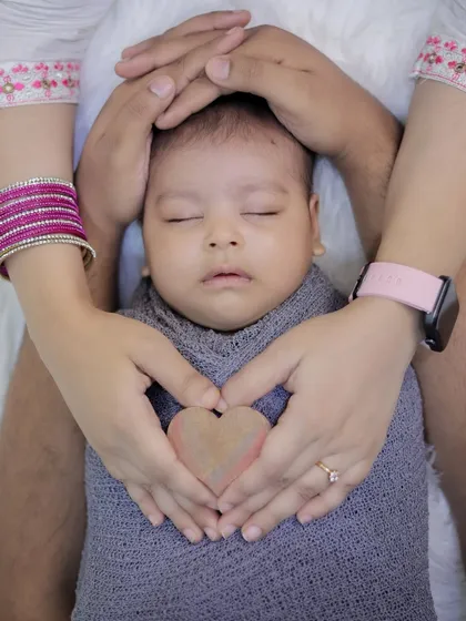 A close up shot showing parents' hands forming a heart around their sleeping newborn. This pose is a beautiful way to symbolize the love and protection surrounding the newest member of the family.