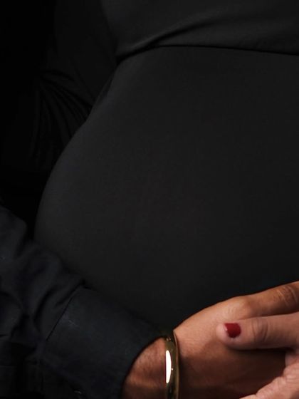 A close-up detail shot of hands on the bump against the black dress. This artistic photo emphasizes the shape of the belly and the protective embrace.