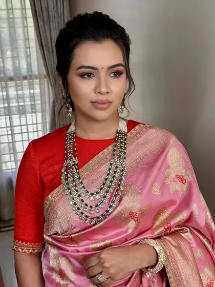 A sophisticated look for a family event, featuring a pink Banarasi saree and a stunning emerald necklace.
