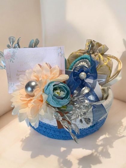 This small, curated hamper in a blue and white rope basket is a sweet and simple gesture. It's decorated with artificial flowers and contains small, thoughtful gifts inside.