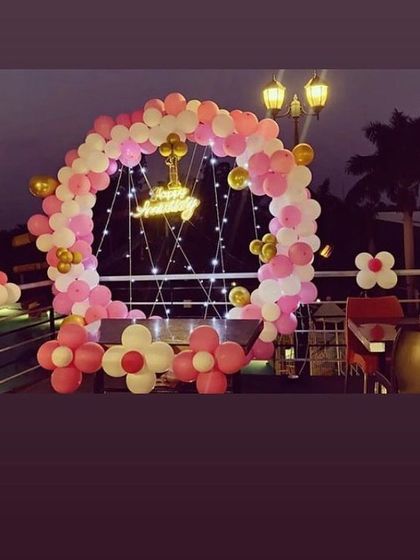 A simple and sweet outdoor birthday setup. This balloon ring in pink, white, and gold is decorated with fairy lights, making it a lovely backdrop for an evening celebration on a terrace.