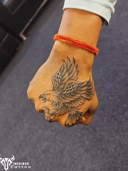 An old, faded set of Om symbols on the hand was completely covered by this powerful black and grey eagle tattoo. The detailed feathers and dynamic pose of the eagle provide excellent coverage and a strong new look.